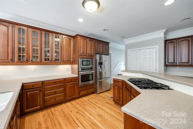 kitchen featuring decorative backsplash, crown molding, appliances with stainless steel finishes, light hardwood / wood-style flooring, and sink