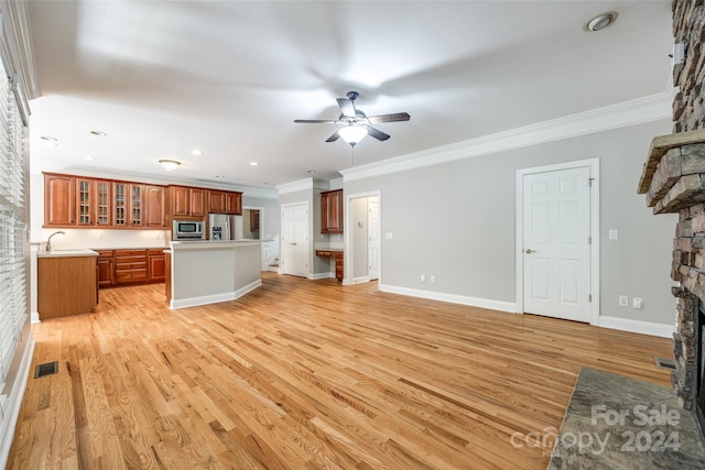 unfurnished living room featuring light hardwood / wood-style flooring, a fireplace, crown molding, ceiling fan, and sink