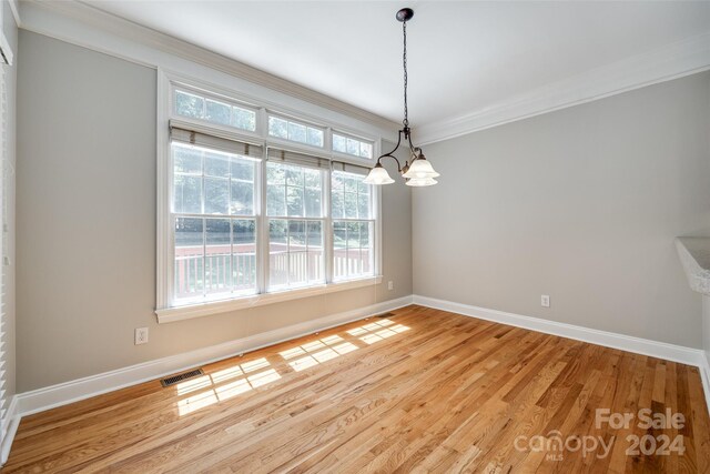 unfurnished dining area featuring a notable chandelier, light hardwood / wood-style flooring, a wealth of natural light, and crown molding