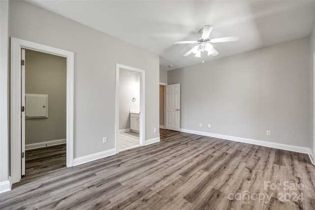 unfurnished bedroom featuring ceiling fan, a walk in closet, ensuite bathroom, and hardwood / wood-style floors