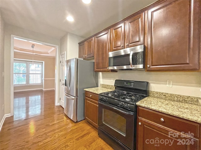 kitchen with a tray ceiling, light stone counters, stainless steel appliances, and light hardwood / wood-style floors