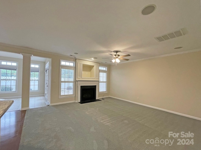 unfurnished living room with ceiling fan, ornamental molding, a wealth of natural light, and carpet floors