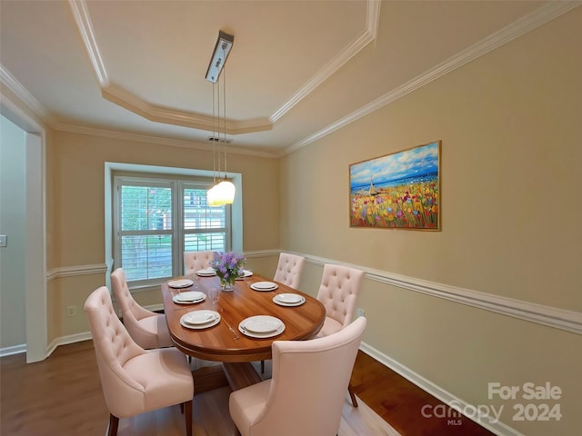 dining area with a tray ceiling, wood-type flooring, and ornamental molding