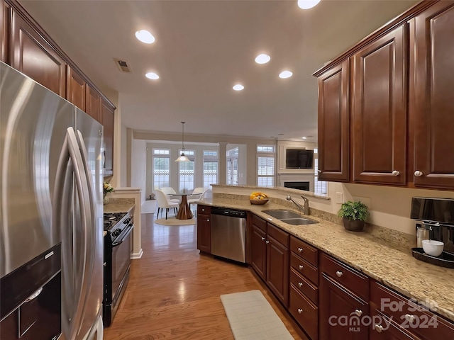 kitchen featuring sink, pendant lighting, light wood-type flooring, appliances with stainless steel finishes, and light stone counters