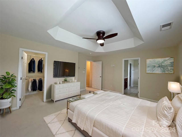 carpeted bedroom featuring a raised ceiling, ceiling fan, a closet, a walk in closet, and ensuite bath