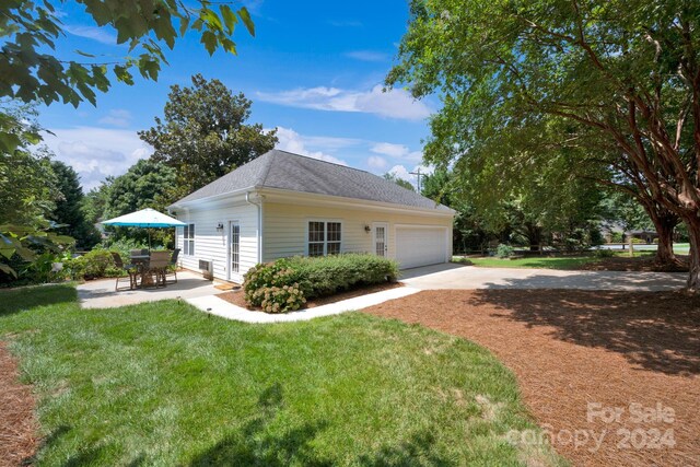 view of property exterior with a garage, concrete driveway, a lawn, a shingled roof, and a patio area