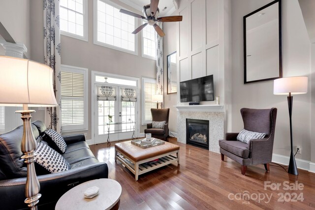 living area featuring plenty of natural light, a glass covered fireplace, ceiling fan, and wood finished floors
