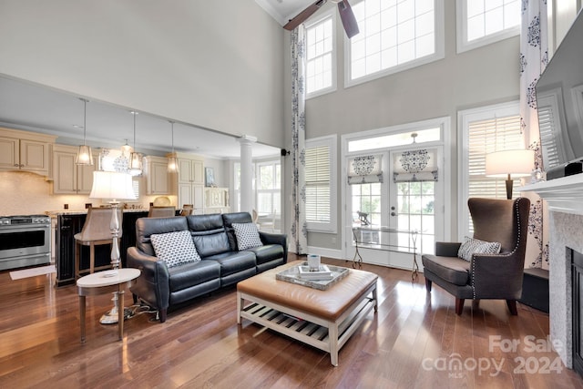 living room featuring ceiling fan, light hardwood / wood-style flooring, crown molding, decorative columns, and a towering ceiling