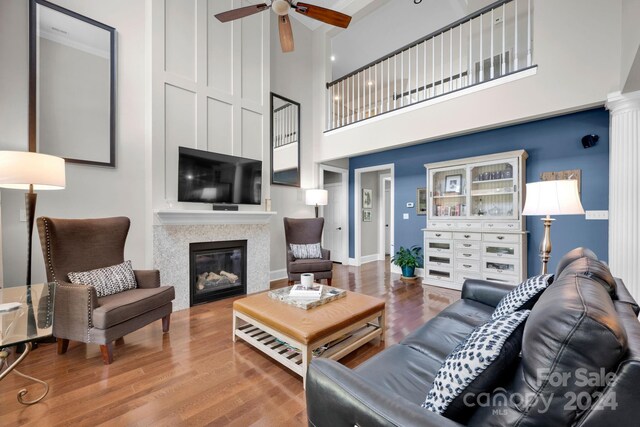 living room featuring baseboards, wood finished floors, a glass covered fireplace, and a ceiling fan