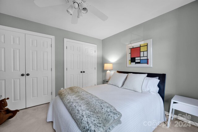 bedroom featuring two closets, light colored carpet, and ceiling fan