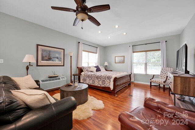 bedroom with a wall unit AC, wood finished floors, baseboards, ceiling fan, and recessed lighting