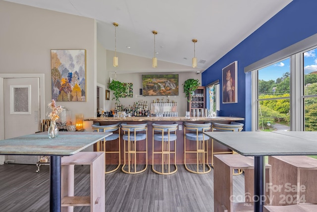 bar featuring bar area, wood finished floors, hanging light fixtures, and vaulted ceiling