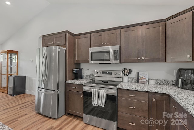 kitchen featuring high vaulted ceiling, light wood-type flooring, dark brown cabinets, light stone countertops, and stainless steel appliances