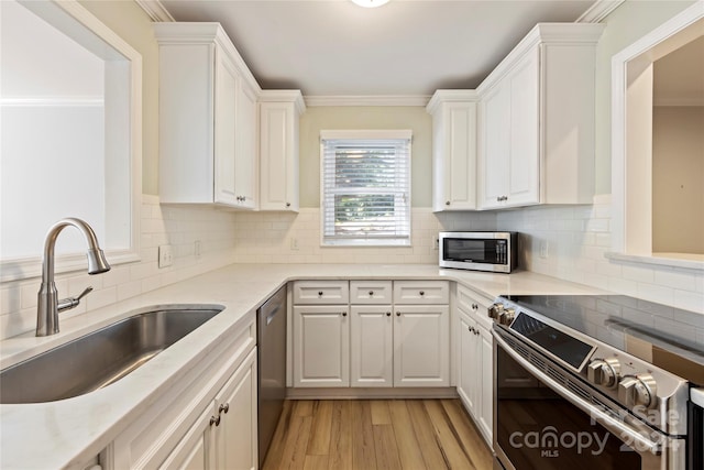 kitchen with tasteful backsplash, white cabinets, sink, appliances with stainless steel finishes, and light hardwood / wood-style flooring