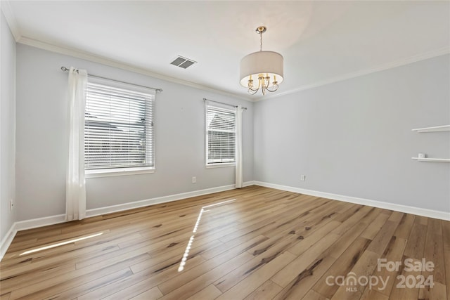 empty room with crown molding, light hardwood / wood-style flooring, and a chandelier