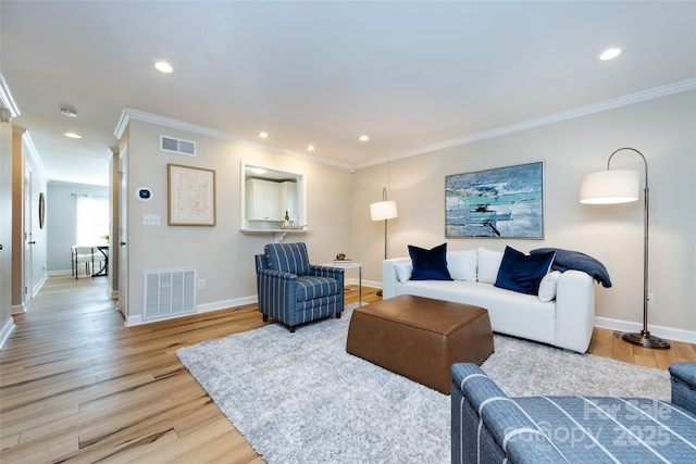 living room featuring ornamental molding, light wood-style flooring, visible vents, and baseboards