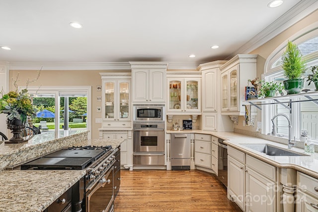 kitchen featuring stainless steel appliances, light hardwood / wood-style floors, light stone countertops, ornamental molding, and sink