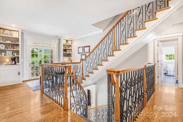 staircase with light wood-type flooring, ornamental molding, and built in features