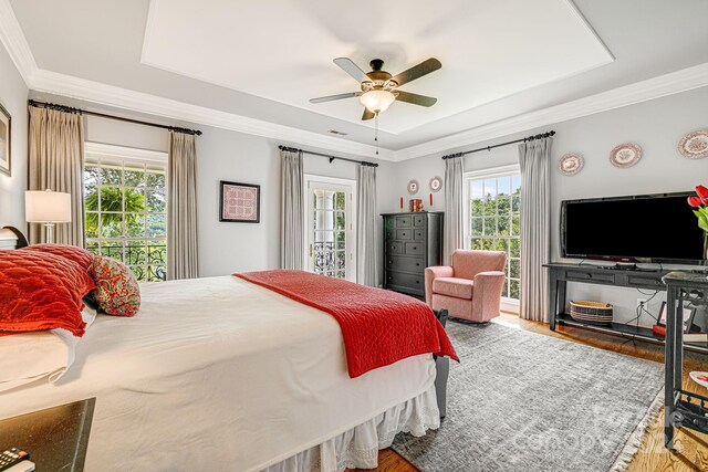 bedroom featuring ceiling fan, wood-type flooring, a raised ceiling, and ornamental molding