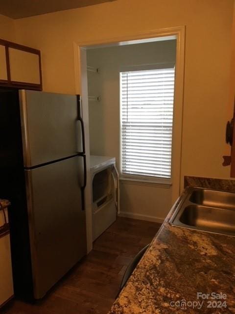 kitchen featuring dark hardwood / wood-style floors, stainless steel fridge, washer / clothes dryer, and dark stone countertops