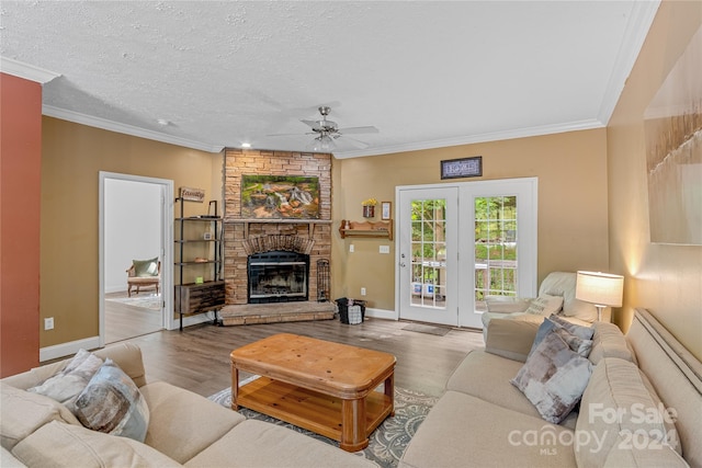 living room with crown molding, a textured ceiling, a large fireplace, ceiling fan, and light hardwood / wood-style floors