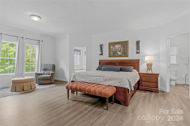 bedroom with a textured ceiling, light wood-type flooring, ornamental molding, and connected bathroom