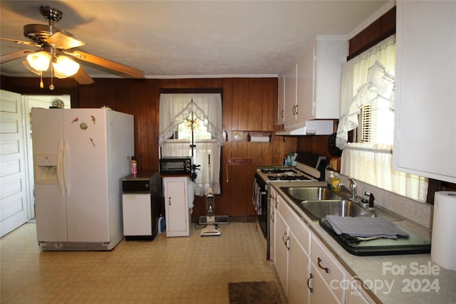 kitchen featuring stainless steel range with gas cooktop, ceiling fan, white fridge with ice dispenser, and wooden walls