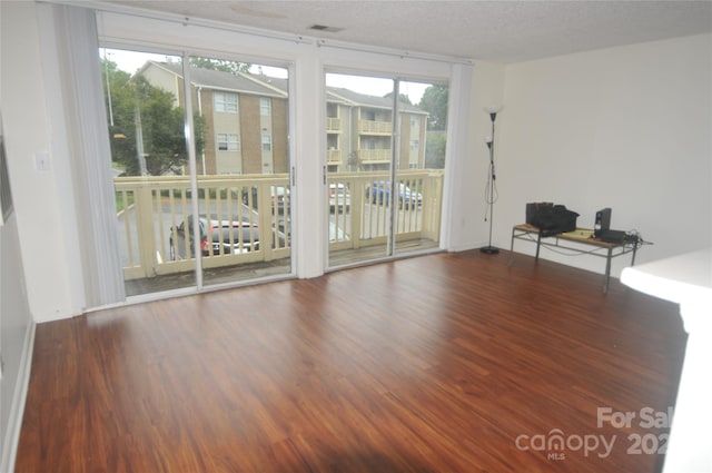 empty room featuring a textured ceiling, hardwood / wood-style floors, and a healthy amount of sunlight