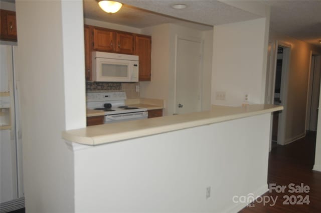 kitchen with backsplash, white appliances, kitchen peninsula, and dark hardwood / wood-style floors