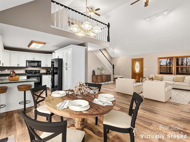 dining space with light hardwood / wood-style flooring, ceiling fan with notable chandelier, rail lighting, and high vaulted ceiling