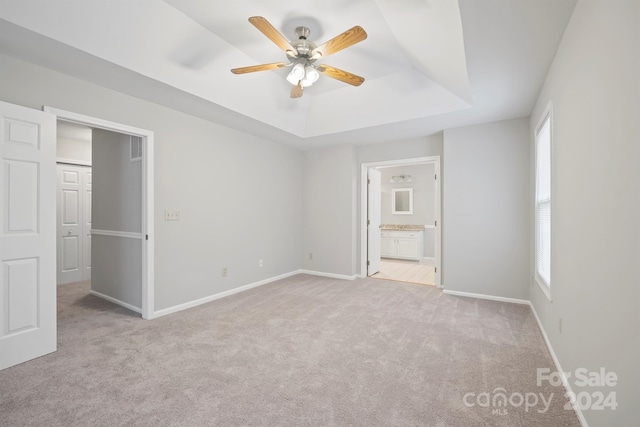 unfurnished bedroom with a closet, light carpet, ceiling fan, and a raised ceiling