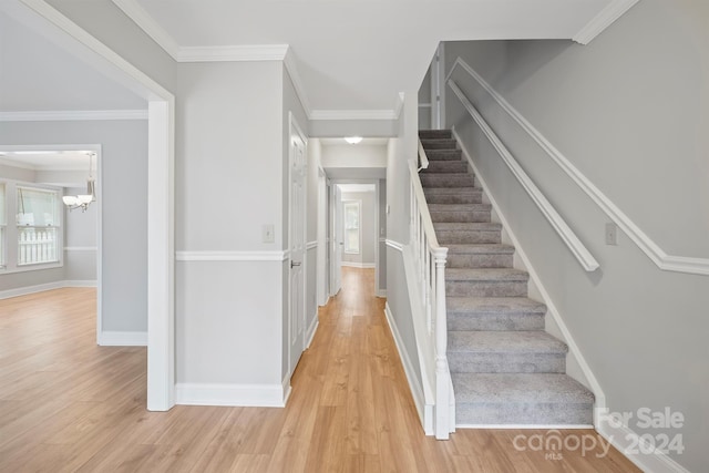 staircase featuring wood-type flooring, crown molding, and a notable chandelier