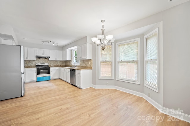 kitchen with stainless steel appliances, white cabinetry, sink, decorative light fixtures, and light hardwood / wood-style flooring