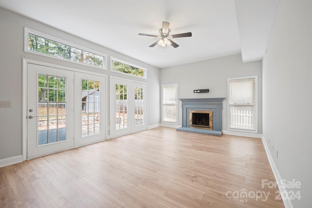 unfurnished living room with a brick fireplace, french doors, ceiling fan, and light wood-type flooring