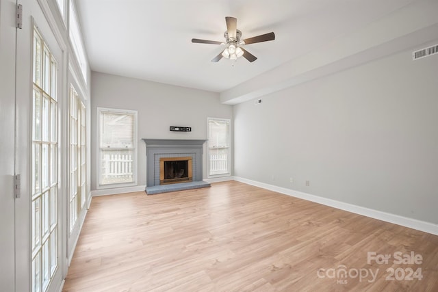 unfurnished living room with ceiling fan, a brick fireplace, and light hardwood / wood-style flooring