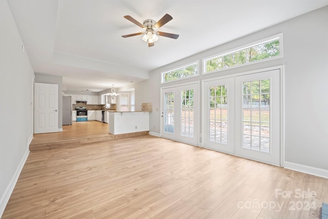 unfurnished living room with ceiling fan with notable chandelier and light hardwood / wood-style flooring