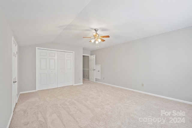 unfurnished bedroom with a closet, lofted ceiling, light colored carpet, and ceiling fan