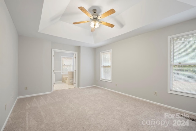 unfurnished bedroom with ensuite bath, ceiling fan, multiple windows, and light colored carpet