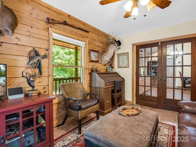 living area with tile patterned floors, wooden walls, french doors, and ceiling fan