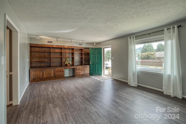 unfurnished living room with dark hardwood / wood-style flooring, a textured ceiling, and track lighting