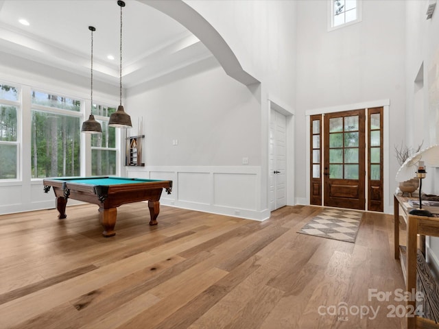 game room with a towering ceiling, billiards, a raised ceiling, and light wood-type flooring