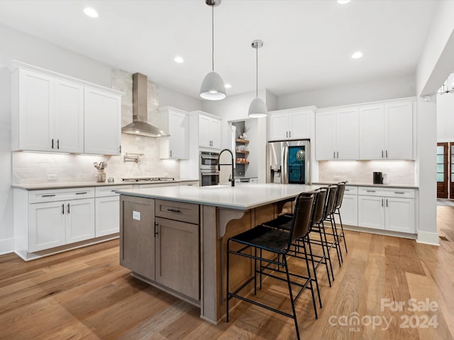 kitchen with white cabinets, stainless steel appliances, a kitchen island with sink, and wall chimney range hood