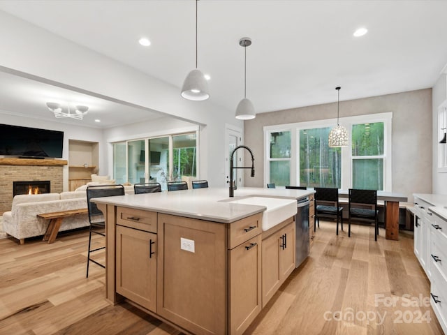 kitchen with decorative light fixtures, dishwasher, an island with sink, sink, and light brown cabinets