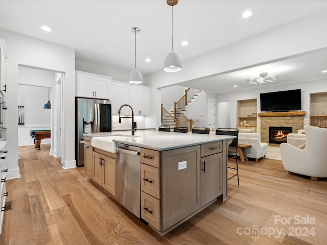 kitchen with a kitchen island with sink, hanging light fixtures, stainless steel appliances, white cabinets, and light wood-type flooring