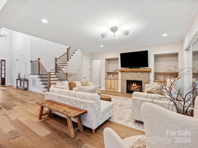 living room with a brick fireplace, an inviting chandelier, built in features, and light wood-type flooring