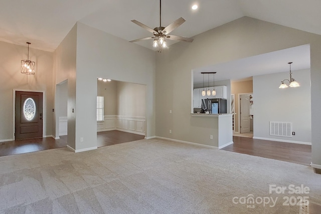 unfurnished living room with ceiling fan with notable chandelier, carpet floors, and high vaulted ceiling