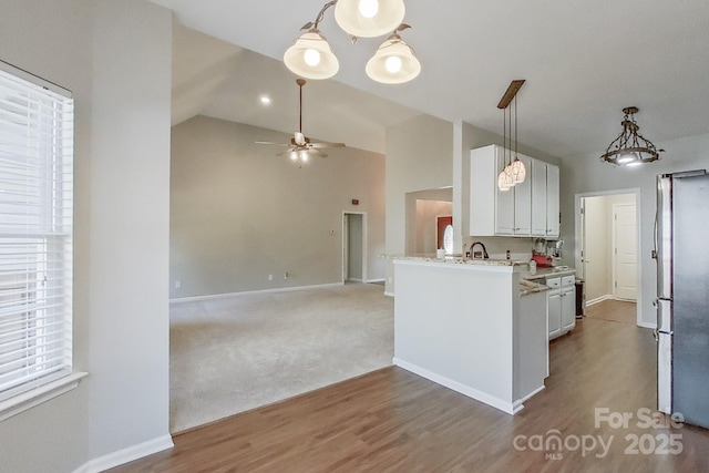 kitchen with white cabinetry, hanging light fixtures, stainless steel fridge, kitchen peninsula, and vaulted ceiling