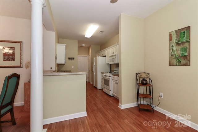 kitchen with hardwood / wood-style flooring, white cabinets, decorative columns, and white appliances