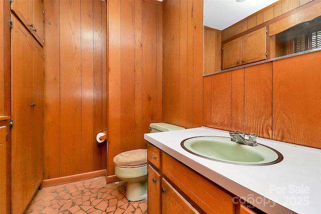 bathroom with toilet, wooden walls, and vanity