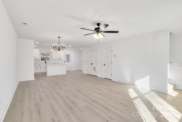 unfurnished living room with ceiling fan with notable chandelier and light hardwood / wood-style floors